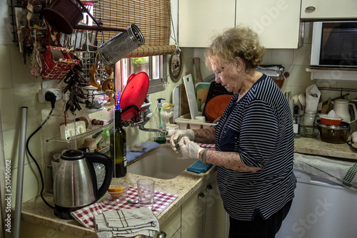Elderly woman washes in her kitchen with rubber gloves.