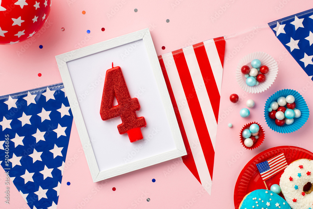 Obraz premium Fourth of July concept. Top view photo of photo frame with number 4 candle US national flag garland paper molds with candies glazed donuts balloons and confetti on isolated pastel pink background