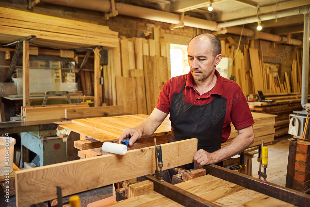 Portrait of a senior carpenter in uniform gluing wooden bars with hand pressures at the carpentry manufacturing Portrait of a senior carpenter in uniform gluing wooden bars with hand pressures at the carpentry manufacturing