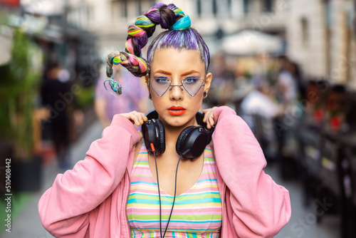 Cool funky young woman with trendy eyeglasses listening music on headphones outdoor photo