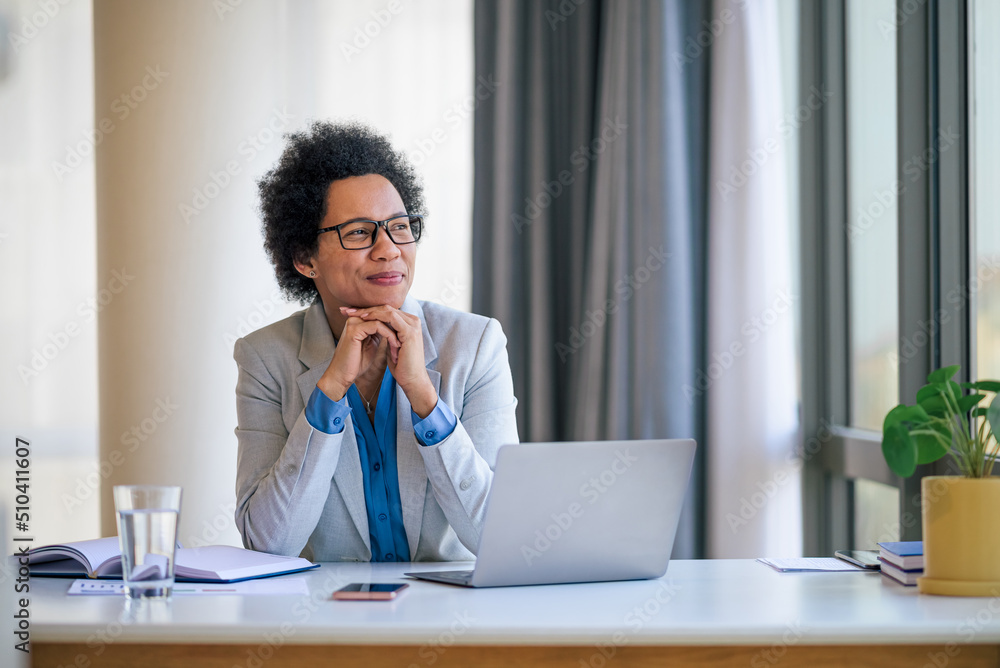 Thoughtful entrepreneur wearing eyeglasses looking through window at desk Thoughtful entrepreneur wearing eyeglasses looking through window at desk