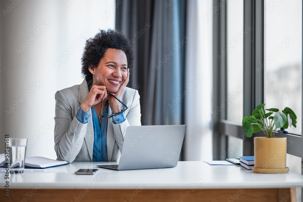 Thoughtful smiling businesswoman looking away while using laptop at office Thoughtful smiling businesswoman looking away while using laptop at office