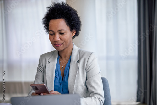 Confident female entrepreneur text messaging on smart phone at office