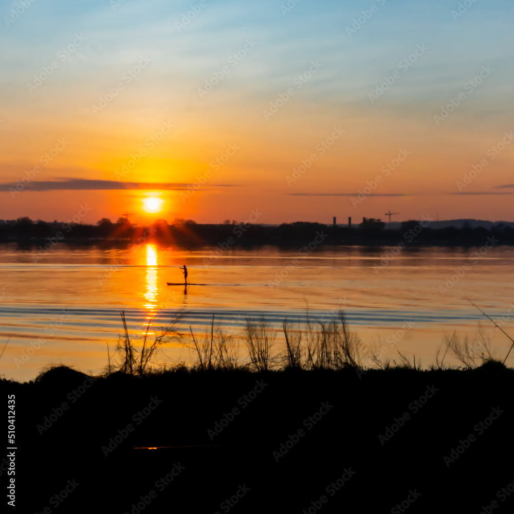 The sun rises over the Potomac river with a paddleboarder in the foreground