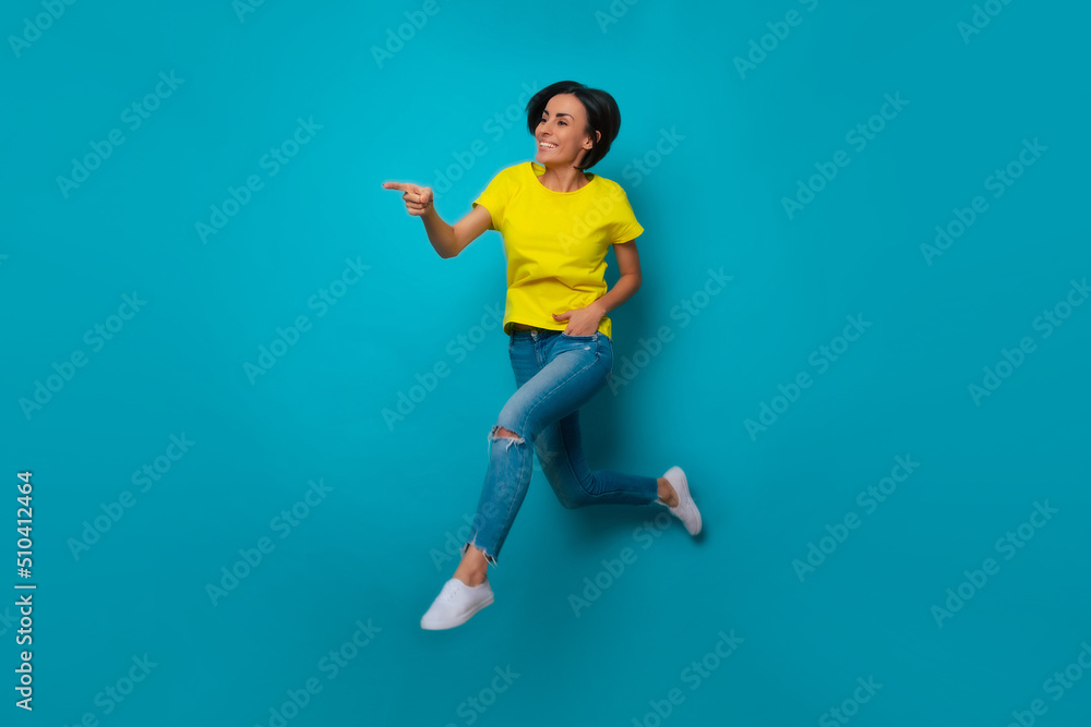 Full-length photo of excited attractive shouting modern woman in yellow t-shirt while she jumping, pointing and moving forward Full-length photo of excited attractive shouting modern woman in yellow t-shirt while she jumping, pointing and moving forward