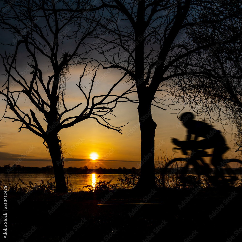 A biker rides on a trail at sunrise with a river in the background.