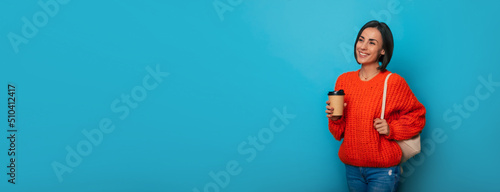 Wide banner photo of happy charming young modern student girl with backpack and coffee cup isolated on blue background with bright toothy smile