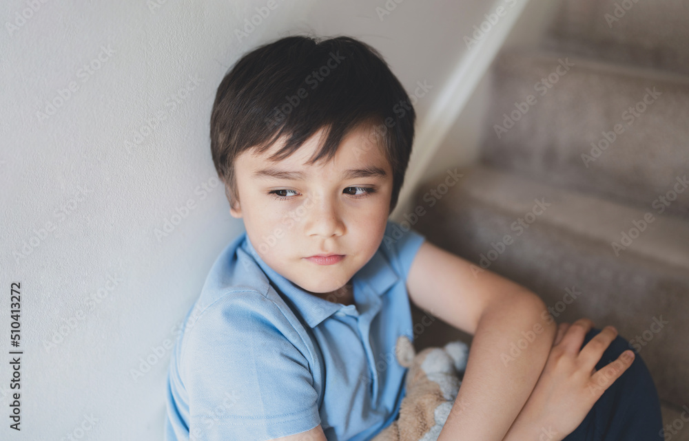 Portrait kid looking out deep in thought, Lonely Child sitting on stairs carpet with thinking face, Childhood and family concept, Emotional child portrait, indoor closeup face Portrait kid looking out deep in thought, Lonely Child sitting on stairs carpet with thinking face, Childhood and family concept, Emotional child portrait, indoor closeup face