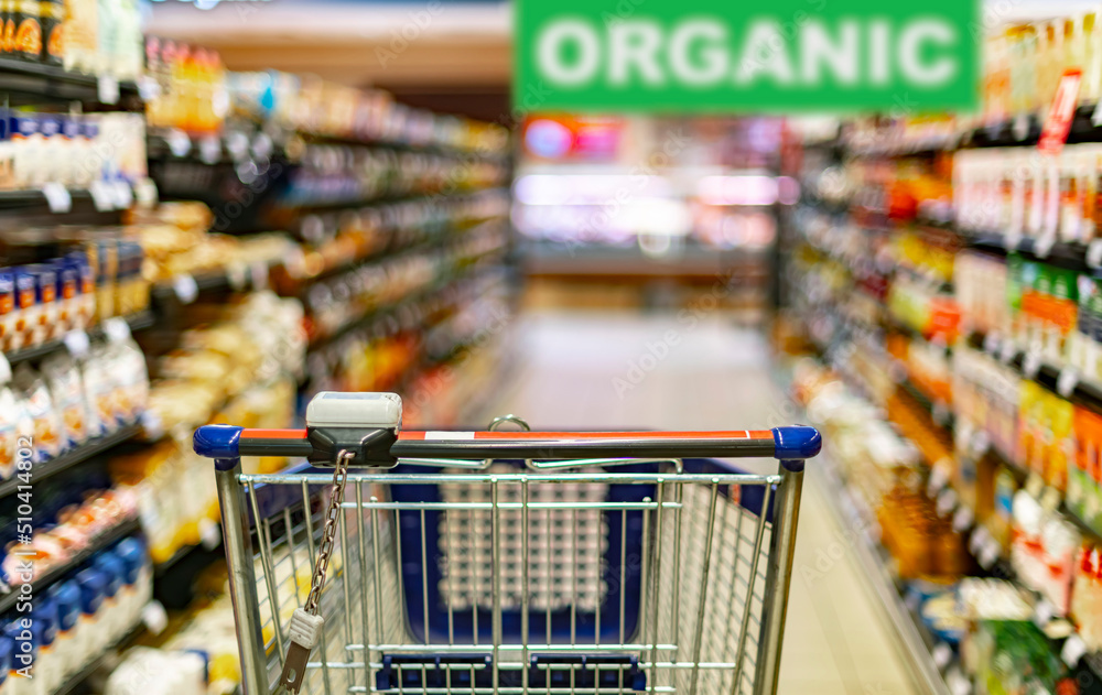 A shopping cart by a store shelf in a supermarket A shopping cart by a store shelf in a supermarket