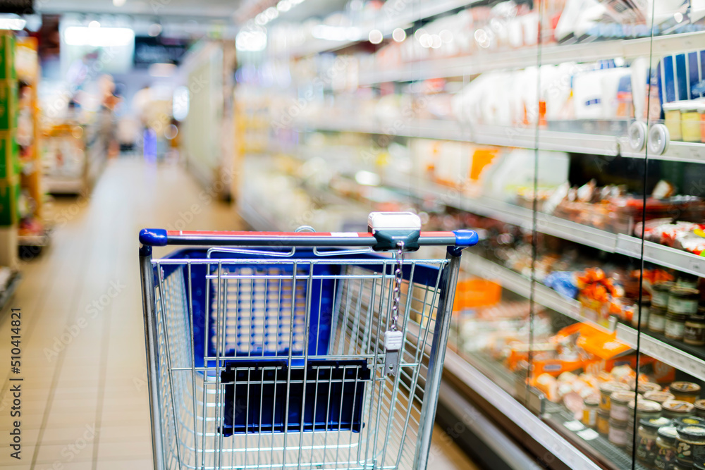 A shopping cart by a store shelf in a supermarket A shopping cart by a store shelf in a supermarket