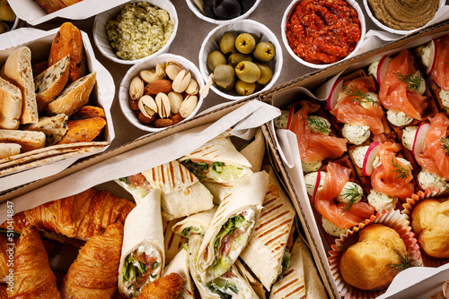 Various snacks in a cardboard box. Set of sandwiches, vegetables, sauces and canapes.
