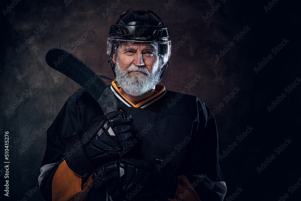 Studio shot of gray haired hockey player dressed in protective sportswear holding hockey stick. Studio shot of gray haired hockey player dressed in protective sportswear holding hockey stick.