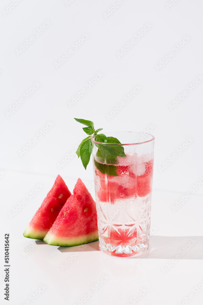 Un vaso de zumo de sandía con trozos de sandia y hielo sobre fondo claro Un vaso de zumo de sandía con trozos de sandia y hielo sobre fondo claro