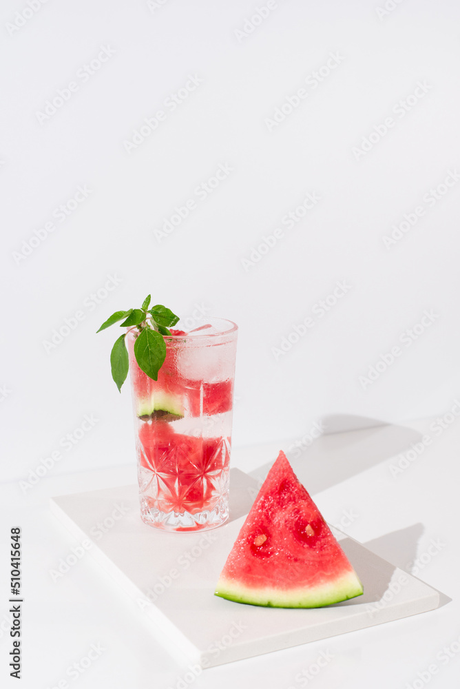 Un vaso de zumo de sandía con trozos de sandia y hielo sobre fondo claro Un vaso de zumo de sandía con trozos de sandia y hielo sobre fondo claro