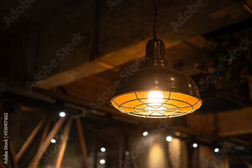 A retro style metal ceiling lighting lamp with warming light glowing bulb. Interior decor, selective focus object. Photo contained some noise and high constrast ratio due to low light condition. photo
