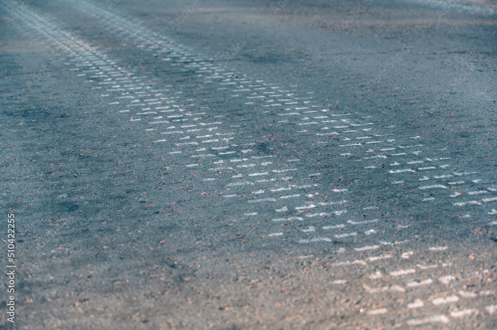 Asphalt road after the passage of the tank. Track marks on a gray road in a receding perspective. Close-up. Selective focus. Asphalt road after the passage of the tank. Track marks on a gray road in a receding perspective. Close-up. Selective focus.