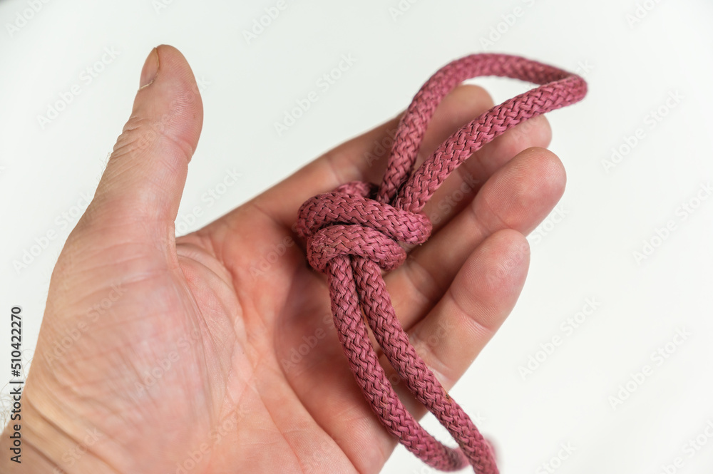 Man holding a red rope in his hand. Neutral background. A round rope with a knot and loop. Close-up. Selective focus.