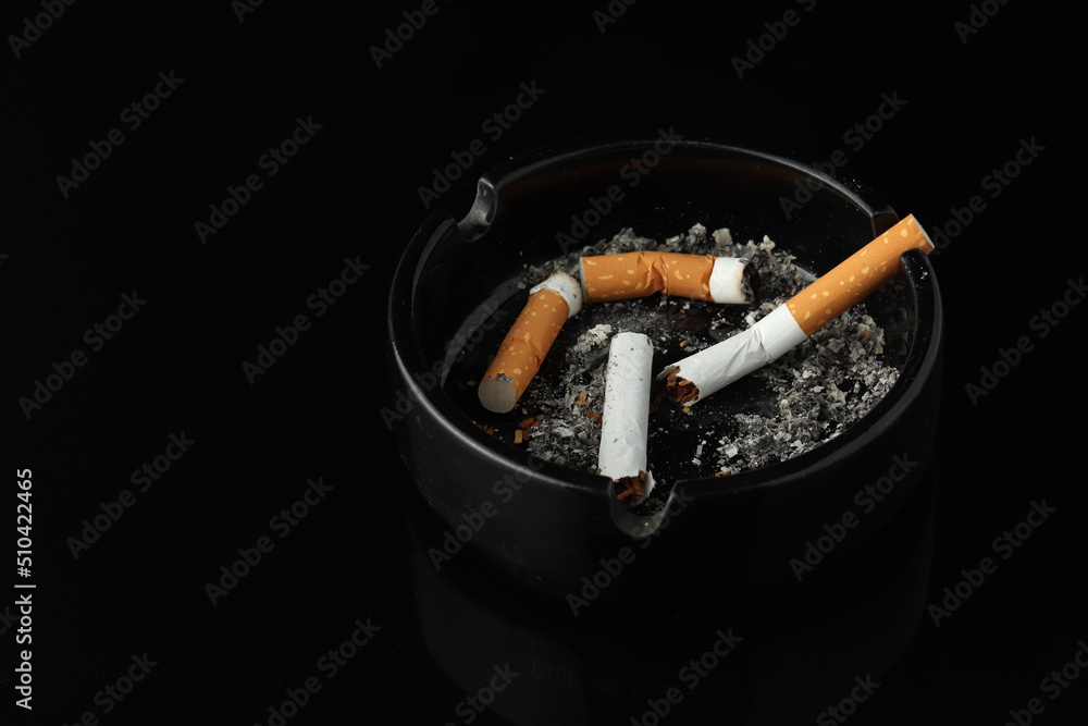 Burning cigarette left in ashtray on black background. Drugs are harmful to the lungs. Burning cigarette left in ashtray on black background. Drugs are harmful to the lungs.