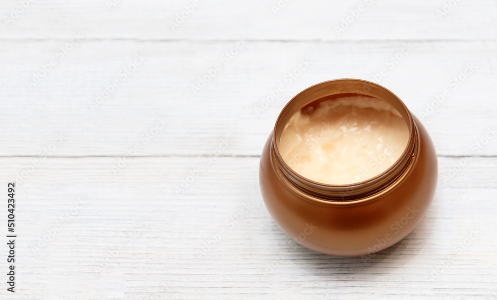Body or face care cream in a round golden jar on a white wooden background with a place for text. Body or face care cream in a round golden jar on a white wooden background with a place for text.