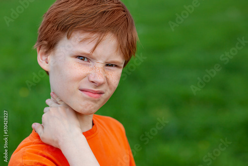 A red-haired boy scratches his neck from a mosquito bite, the child winces against the background of nature. Spray against mosquitoes and insects.