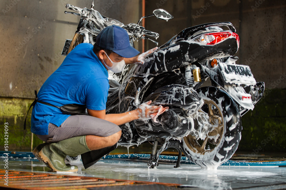 Worker washing a motorbike with foam soap in car wash station. Stock Photo Adobe Stock