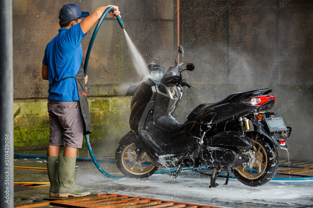 Worker using a hose for detailed cleaning. Spraying and washing a motorbike in professional car