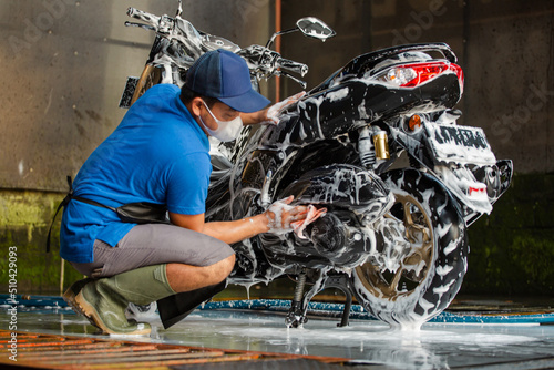 Worker washing a motorbike with foam soap in car wash station.