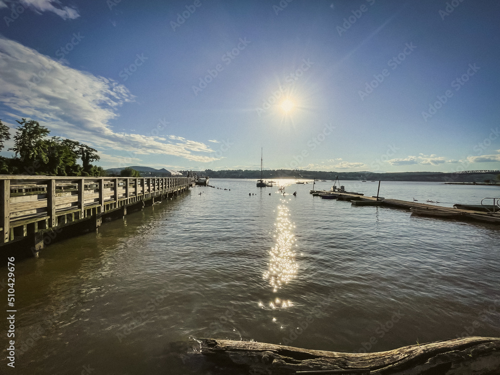 Fototapeta premium Beacon, NY - USA - June 11, 2022 Landscape view of sunset over the Scenic Hudson's Long Dock Park, located on the bank of the Hudson River at Beacon, NY. Boats and the city of Newburgh can be seen.