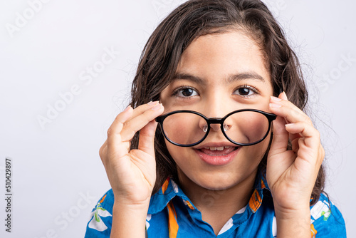 Cuadro en lienzo Image of a small boy in a blue shirt, looking at the camera while putting on his glasses, with a white background