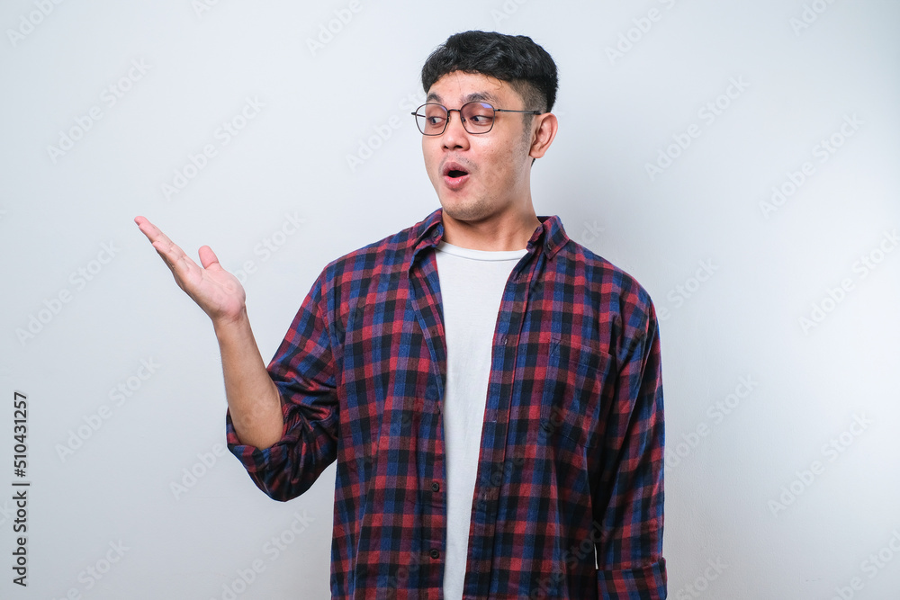 Young asian chinese man Surprised pointing with hand finger to the side, open mouth amazed expression. Young asian chinese man Surprised pointing with hand finger to the side, open mouth amazed expression.