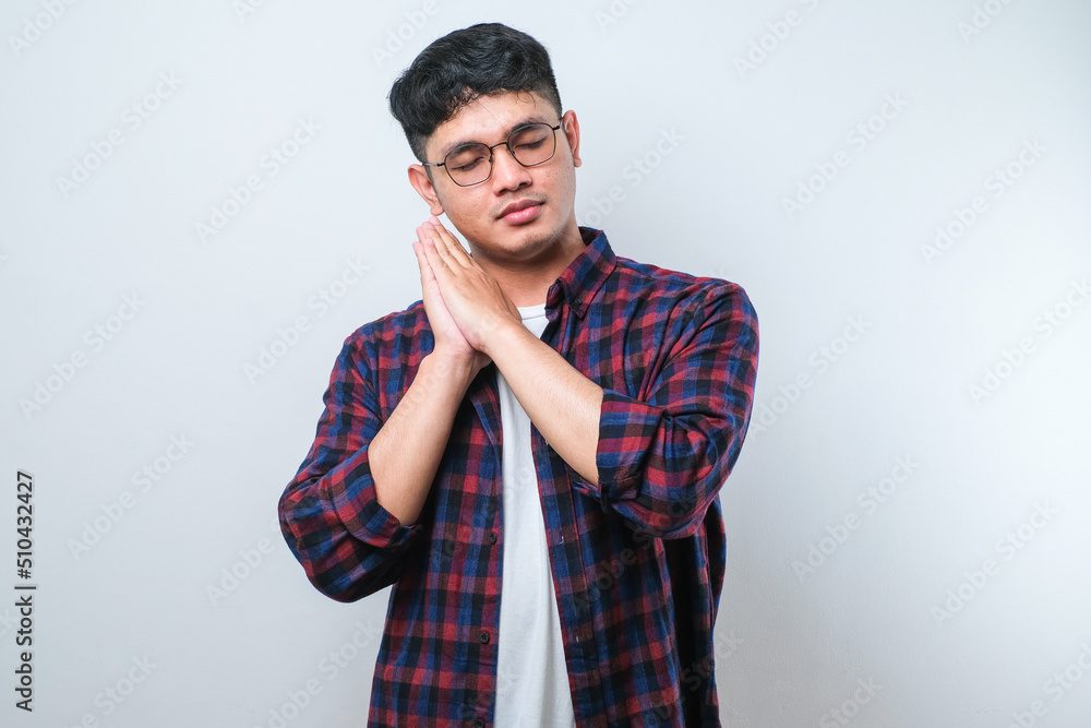 Asian handsome man wearing shirt sleeping tired dreaming and posing with hands together while smiling with closed eyes Asian handsome man wearing shirt sleeping tired dreaming and posing with hands together while smiling with closed eyes