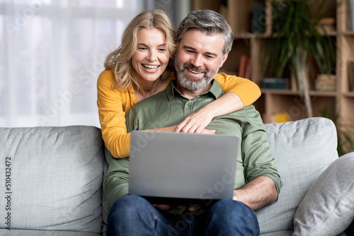 Portrait Of Happy Middle Aged Couple Using Laptop At Home