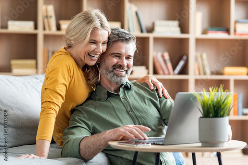 Happy middle aged couple websurfing on laptop together while relaxing at home photo