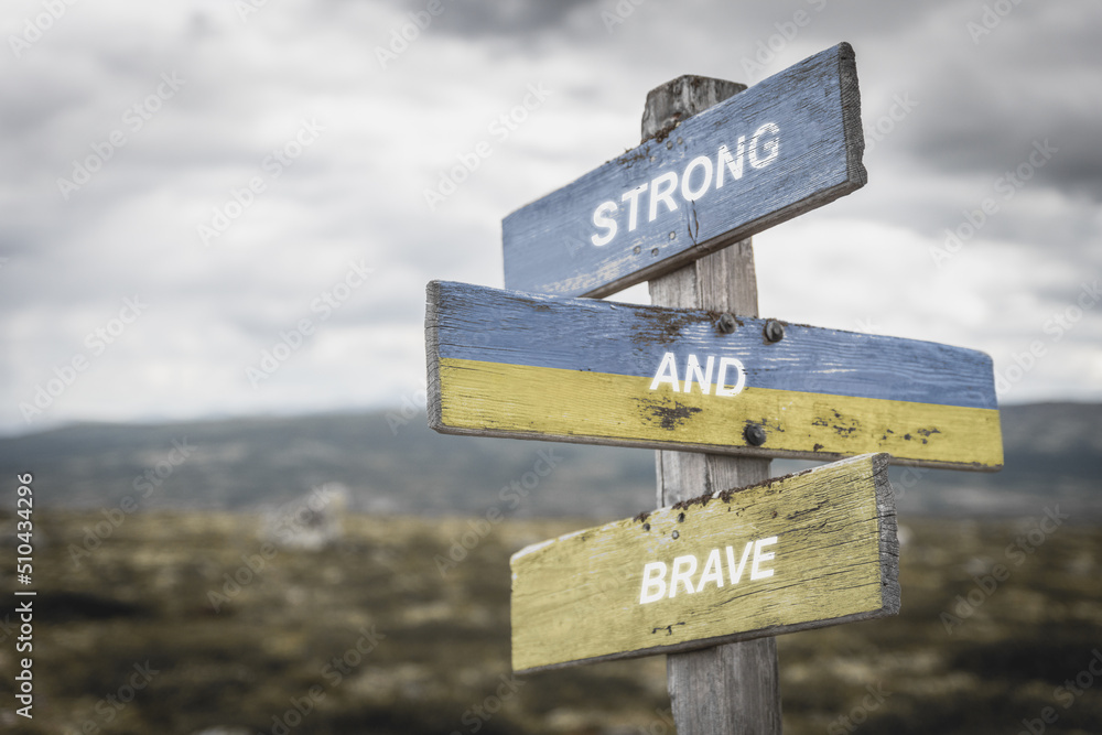 strong and brave text quote on wooden signpost outdoors in nature. War in ukraine concept.