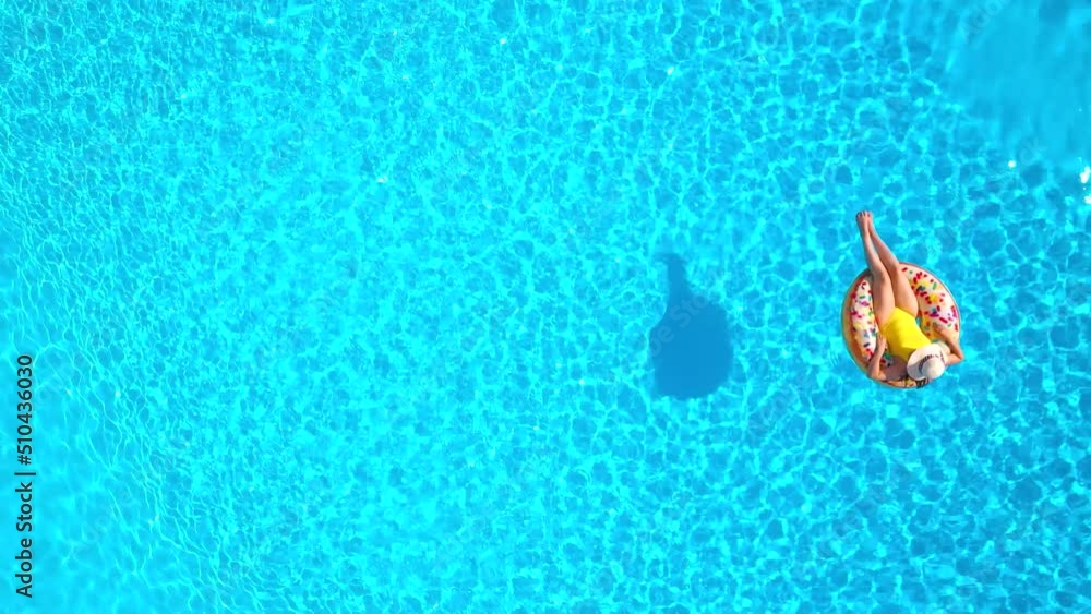 Aerial view of a woman in yellow swimsuit lying on a donut in the pool
