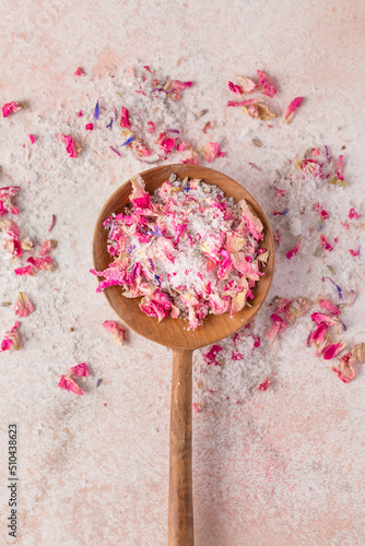 See salt wih with dried flower petals in wooden scoop on pink marble table