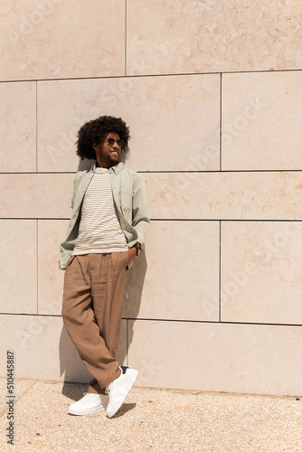Relaxed Black man outdoor. African American man in casual clothes and sunglasses walking on sunny day. Portrait, city life concept