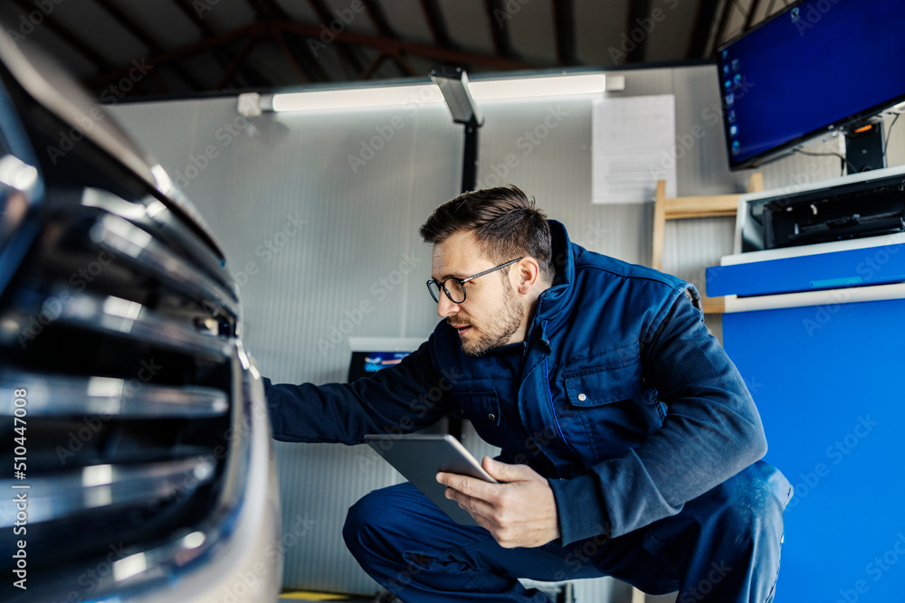 A car service worker crouching and using tablet to check on the car at service. A car service worker crouching and using tablet to check on the car at service.