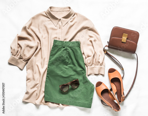 Women's clothing - blouses, bermuda shorts, leather sandals pumps, cross body bag on a light background, top view