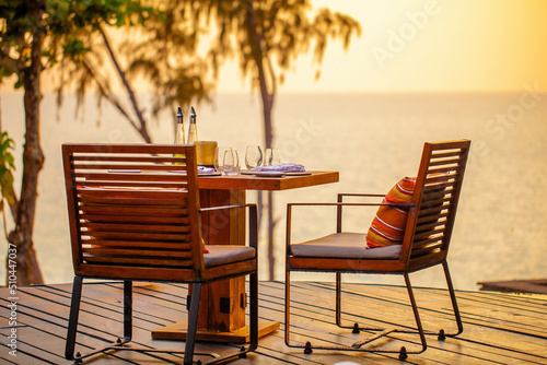 Sea sunset in modern luxury restaurant with terrace. Outdoor restaurant at the beach with pair of chair. Table setting at tropical beach restaurant. Elegant hotel or resort restaurant.
