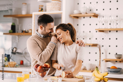 Happy couple cuddling in kitchen at home and preparing healthy fruit snack.