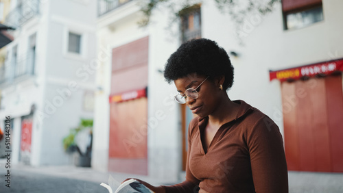 African American woman in glasses sitting on the street and read