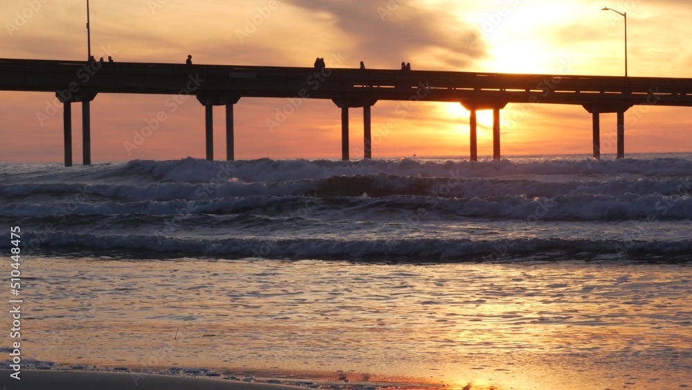 Silhouette of people walking, pier on piles in sea water. Ocean waves, dramatic sky at sunset. California coast aesthetic, beach or shore vibe at sundown. Summer seascape in San Diego near Los Angeles Silhouette of people walking, pier on piles in sea water. Ocean waves, dramatic sky at sunset. California coast aesthetic, beach or shore vibe at sundown. Summer seascape in San Diego near Los Angeles