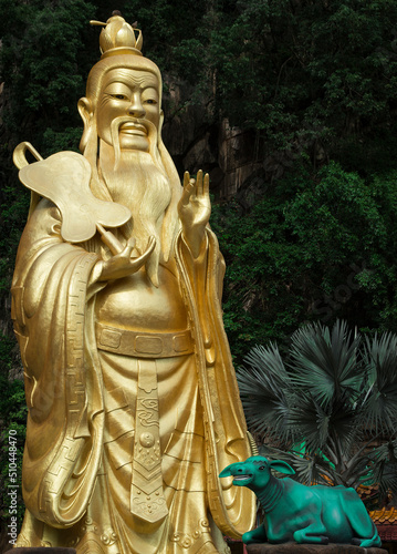 Gold colour of Daode Tianzun statue at the temple, beside the rainforest/mountain.