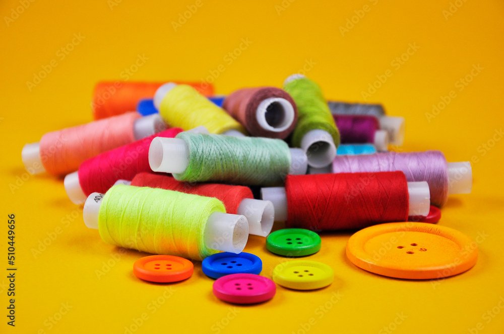 Set of buttons and Spools with multicolored threads on a yellow background. Blurring background. Set of buttons and Spools with multicolored threads on a yellow background. Blurring background.