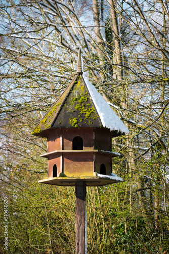Hexagonal wooden bird house and feeder with Spring snow in bright sunshine