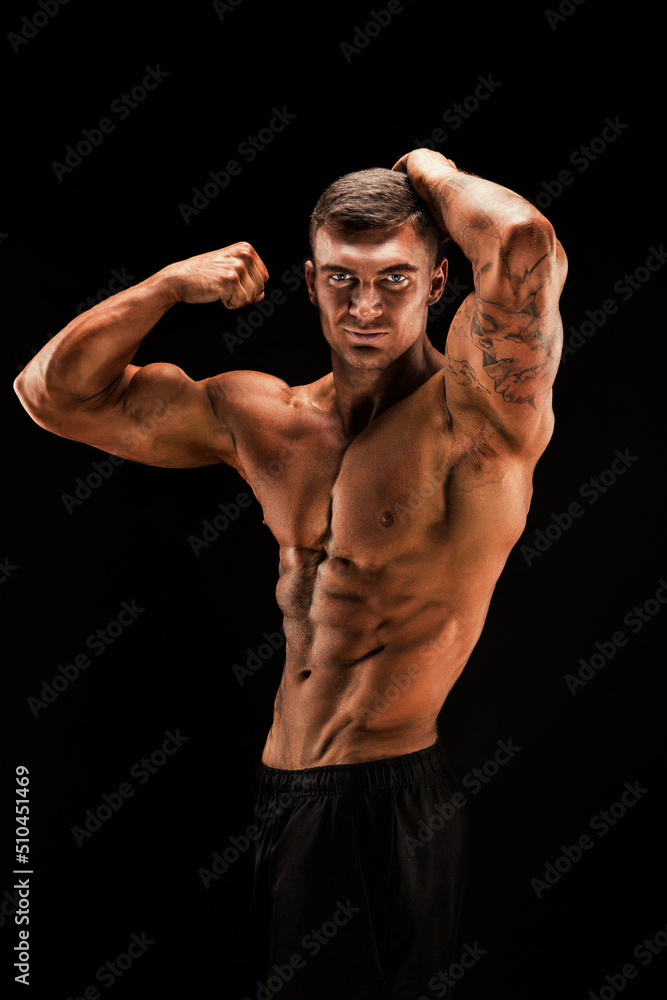 Handsome power athletic man confidently looking forward. Strong bodybuilder with six pack, perfect abs, shoulders, biceps, triceps and chest Isolated on black background