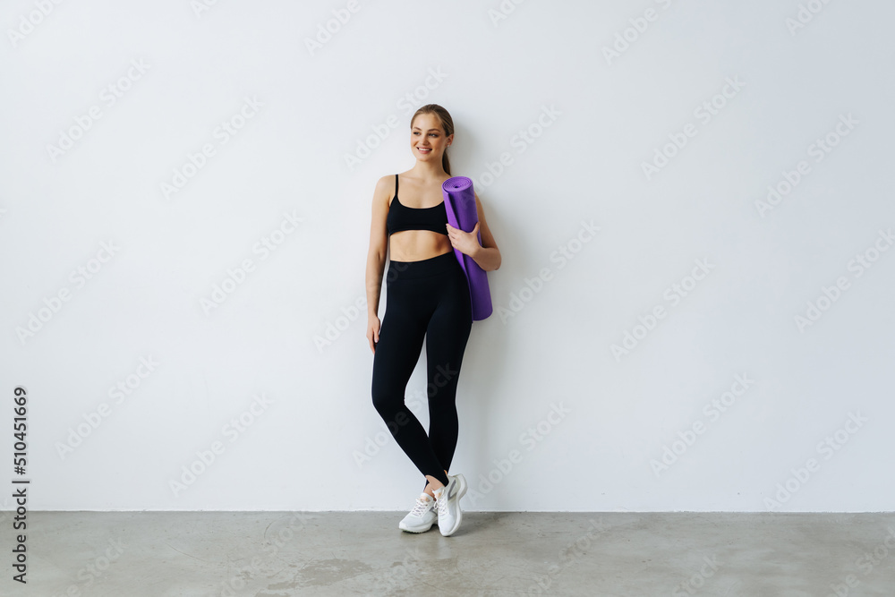 Young woman holding a yoga mat, isolated in a white background Young woman holding a yoga mat, isolated in a white background