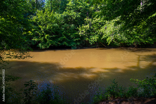 a gorgeous summer landscape in the park with the silky brown waters of Little River surrounded by lush green trees, grass and plants with blue sky and clouds at Olde Rope Mill Park in Woodstock photo