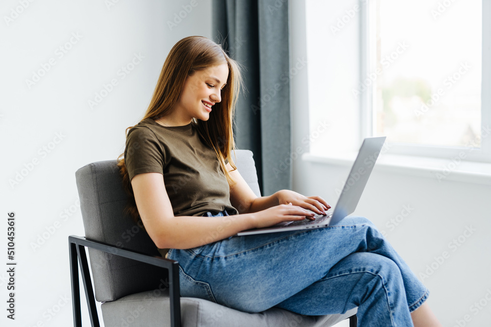 Young woman sitting on chair with laptop at home Young woman sitting on chair with laptop at home